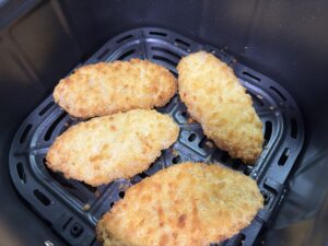 コソリ（ノンフライヤー）のバスケットの中で、白身魚のフライがこんがりと、美味しそうな黄金色に焼き上がった状態。 事前の「油くぐらせ」効果で、衣はサクサク、中身はふっくらと仕上がっています。大量の油で揚げるよりも大幅にカロリーをカットでき、キッチンが油で汚れる心配もない、ヘルシーで快適な調理の成果です。